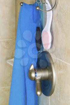Vertical photo of shower accessories consisting of wash cloth, scrubbers, hanging basket, faucet with shower wall in background 