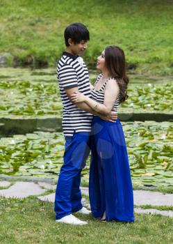 Vertical photo of young adult couple looking at each other with pond in background 
