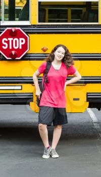 Vertical photo of young girl standing by side of bus, with back pack over her shoulders, while looking forward
