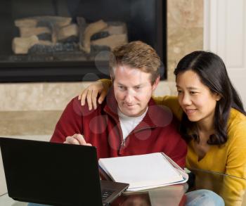 Photo of close mature couple looking at information on the computer screen together with fireplace in background  