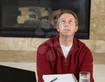 Photo of mature man looking up in frustration while work from home with fireplace in background  
