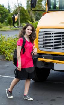 Vertical photo of young girl walking in front of bus, with back pack over her shoulders, while looking forward