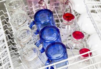 Horizontal photo of dishwasher loaded with blue, red, clear and pink glasses with white bowls