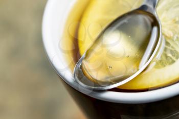 Horizontal closeup photo of golden honey, in spoon, with fresh lemon slice in hot cup of tea