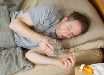 Horizontal photo of mature man preparing to take his medicine with water while lying in bed 