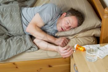 Horizontal photo of mature man trying to reach for his medicine while lying in bed 