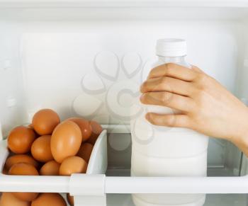Photo of female hand grabbing milk container off of refrigerator door shelf with organic eggs off to the side 