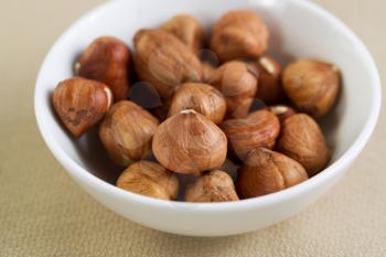 Closeup horizontal photo of a bowl filled with raw whole nuts lying on top of a textured table cloth 