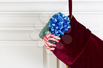 Horizontal photo of Christmas stocking hanging from fireplace mantle with real candy canes and packaged gift hanging outside