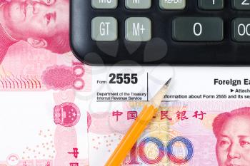 Horizontal photo of partial IRS Income tax form 2555, for Foreign Earnings from outside the United States, pencil and calculator with Chinese Currency in background 