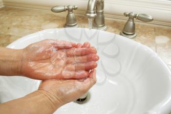 Horizontal photo of female hands lathering in liquid soap with bathroom sink and running faucet in background 