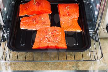 Horizontal photo of Wild Red Salmon pieces coated with dried red peppercorns and sea salt inside oven with stone counter top underneath 