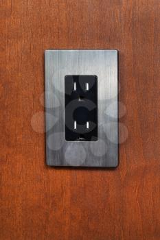 Vertical photo of an electrical outlet and face plate on cherry wood wall 