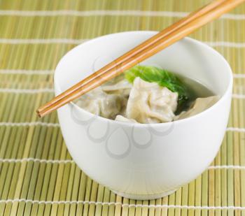 Close up photo of freshly made wonton with chopsticks on top of white bowl 