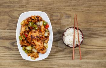 Overhead view of Chinese spicy chicken dish and rice in bowl with chopsticks placed on rustic wooden boards.  