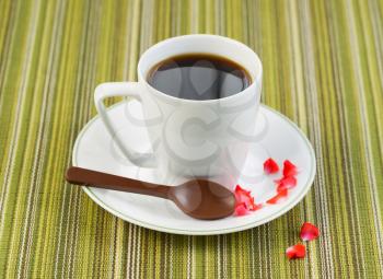Closeup photo of black coffee, in small cup, with chocolate spoon, red rose petals on saucer 