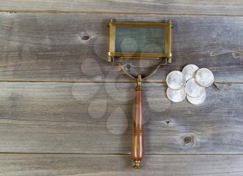 Horizontal view of an old rectangular shaped magnifying glass and a pile of old silver dollar coins on rustic wood 