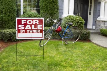 Closeup view of Modern Suburban Home with for Sale Real Estate Sign in front yard and bicycle and house in background 