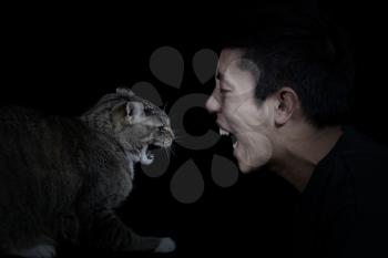 Close up of a Cat and Man showing anger towards each other on black background with light on faces
