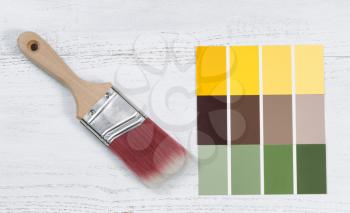 Close up of a new paint brush and paint color choice templates on white wooden boards