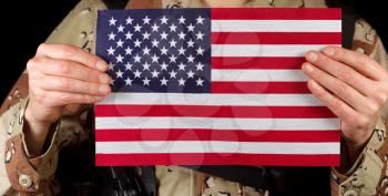 Close up horizontal image of United States of America flag with armed male soldier holding it while on black background. 
