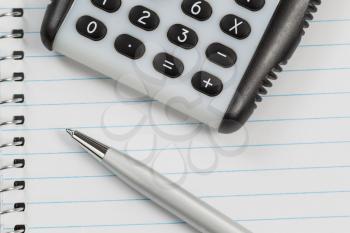 Close up shot of hand held calculator, silver pen and notepad in horizontal layout. 