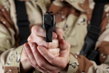 Close up horizontal image of pistol, pointing forward, with armed male soldier in background. Focus on front part of weapon with soldier blurred out. 