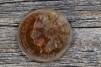 Close up shot of Indian Head Cent, uncirculated condition, on aged wood. Coin showing red and brown colors from copper metal aging process. First one cent that was legal tender by the coinage act of 1