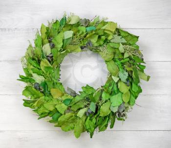 Top view angled shot of seasonal wreath made of green leaves on white aged wood