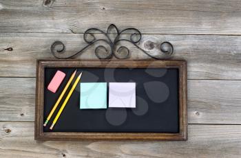 Old fashion chalkboard, pencils, eraser and paper notes on rustic wood. Layout in horizontal format.