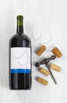 Vertical image a large bottle of red wine with an antique corkscrew with old corks on white wood. 
