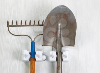 Close up image of garden tools hanging from rack on white wood.
