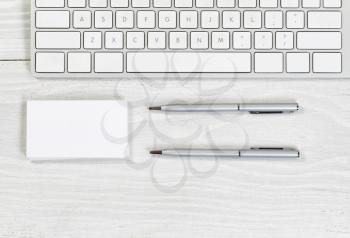 Image of partial keyboard, stack of blank business cards, and silver pens on white desktop. Layout in horizontal format.