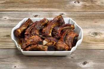 Large plate filled with delicious baked barbecued ribs on rustic wood. 