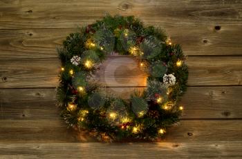 Christmas wreath with white lights on rustic wooden boards.  Low lighting to bring out glow of lights. 