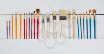 High angled view of brand new paint brushes organized on white wood. Layout in horizontal format.
