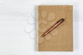 Vintage metal pen and burlap covered notepad on white wooden desktop.