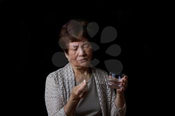 Senior woman preparing to take her medicine with water. Black background.