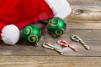 Close up of Santa Claus hat, green ornaments and candy canes on rustic wood