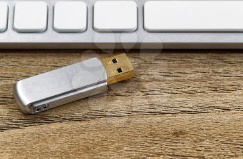 Selective focus on data thumb drive with partial keyboard in background. Layout in horizontal format on rustic wood. 