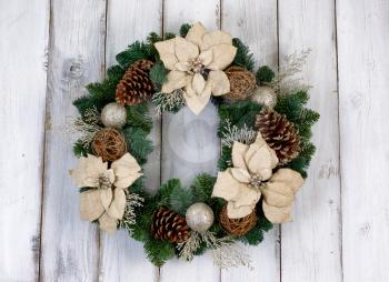 White Poinsettia flower and pine cone Christmas wreath on rustic white wood. 
