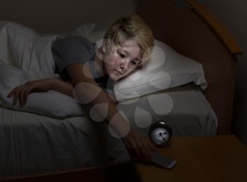 Teenage girl reaching for her cell phone, on night stand, while in bed. Teen using technology late at night instead of sleeping. 