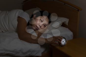 Woman with insomnia touching alarm clock while eyes open. Select light and focus on woman and clock with darker background for night time concept.