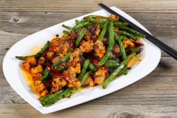 Close up view of crispy fried chicken pieces with green beans and Chile peppers on rustic wood setting. 