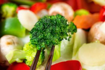 Freshly cooked vegetables with chopsticks. Filled frame format with selective focus on front broccoli between chopsticks.  