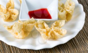 Close up view of crispy fried wanton treats with dipping sauce in background. Selective focus on front shells. 