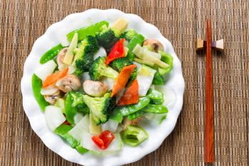 Top view of steamed mixed vegetables in large plate with bamboo mat underneath. 