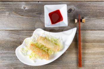Top view of crispy spring rolls with dipping sauce and chopsticks in holder on rustic wooden boards. 