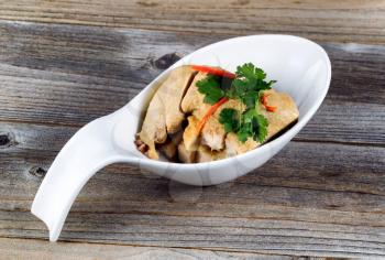 Close up of sliced chicken and herbs in spoon shaped bowl on rustic wood. 