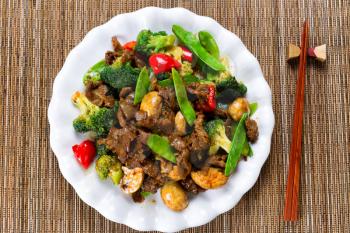 High angle view of tender beef slices, mushrooms, broccoli, peppers and peas in white plate. 